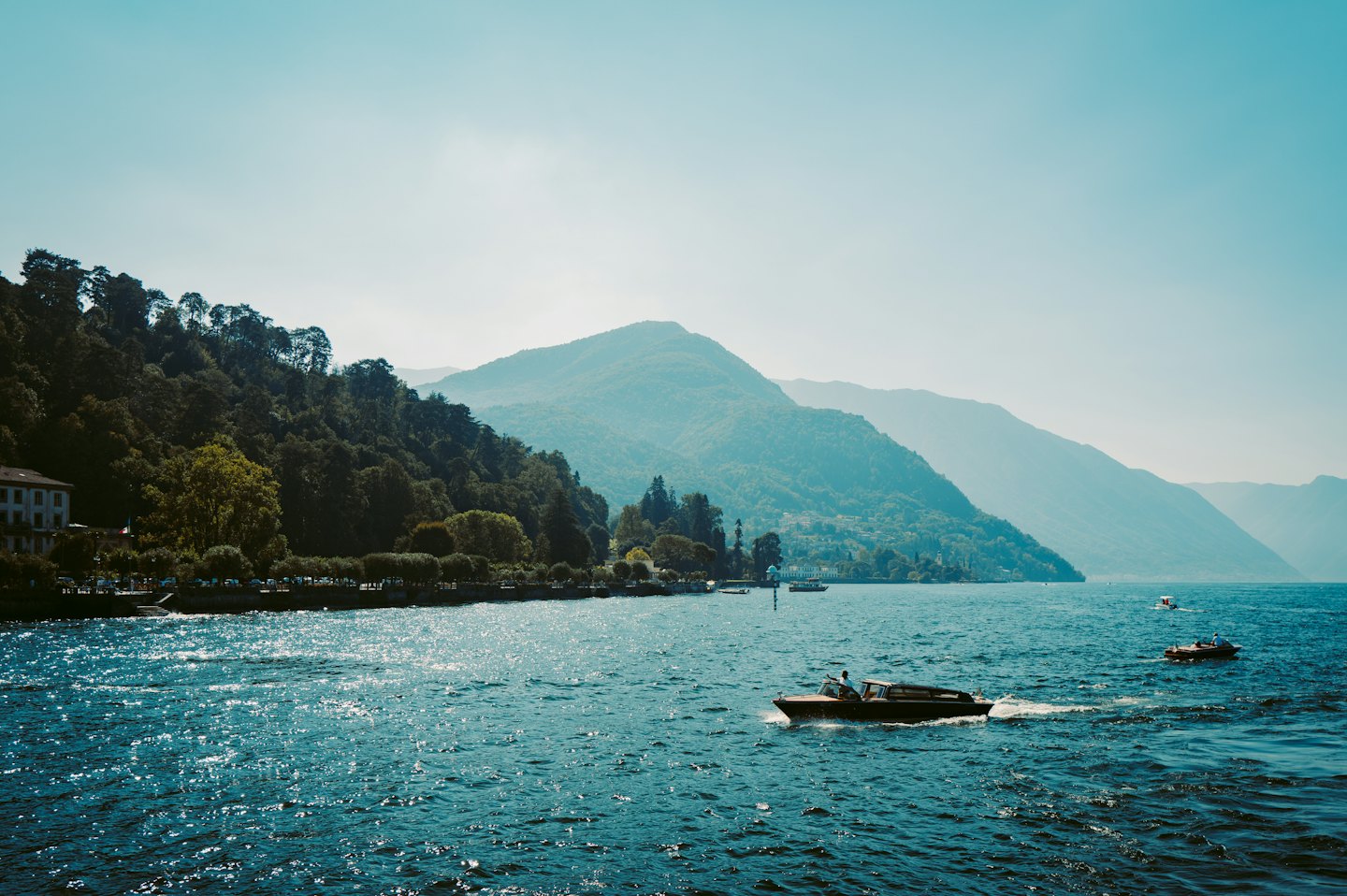 Speedboat with one person cruises across blue water near mountains.
